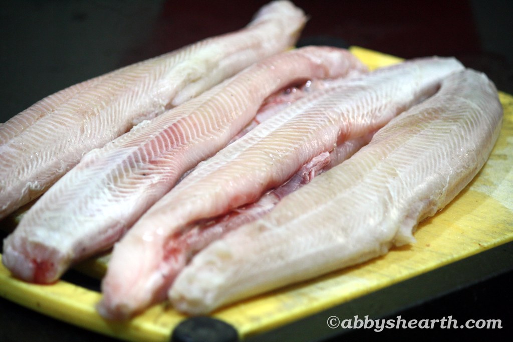Raw fish fillets of milk shark on a yellow cutting board.