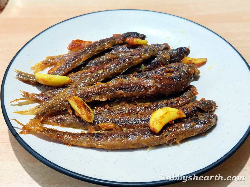 Crispy fried kalenta fish garnished with garlic slices on a white plate.