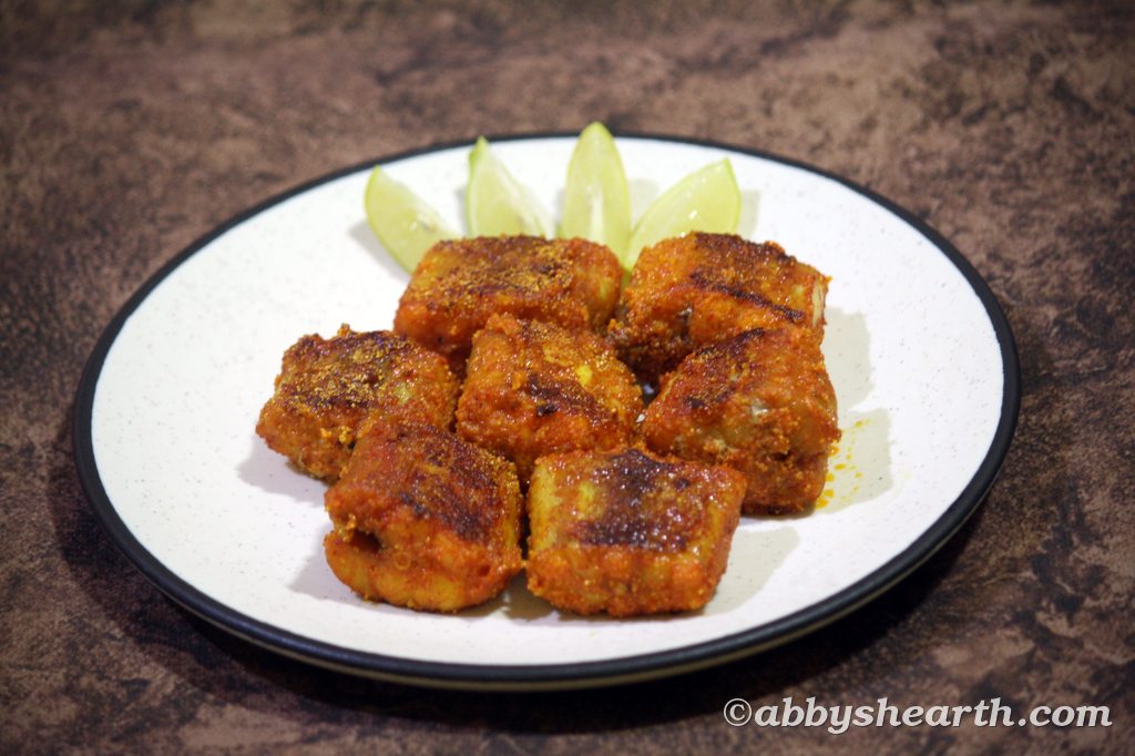 Crispy fried shark fish pieces served with lemon wedges on a white plate.