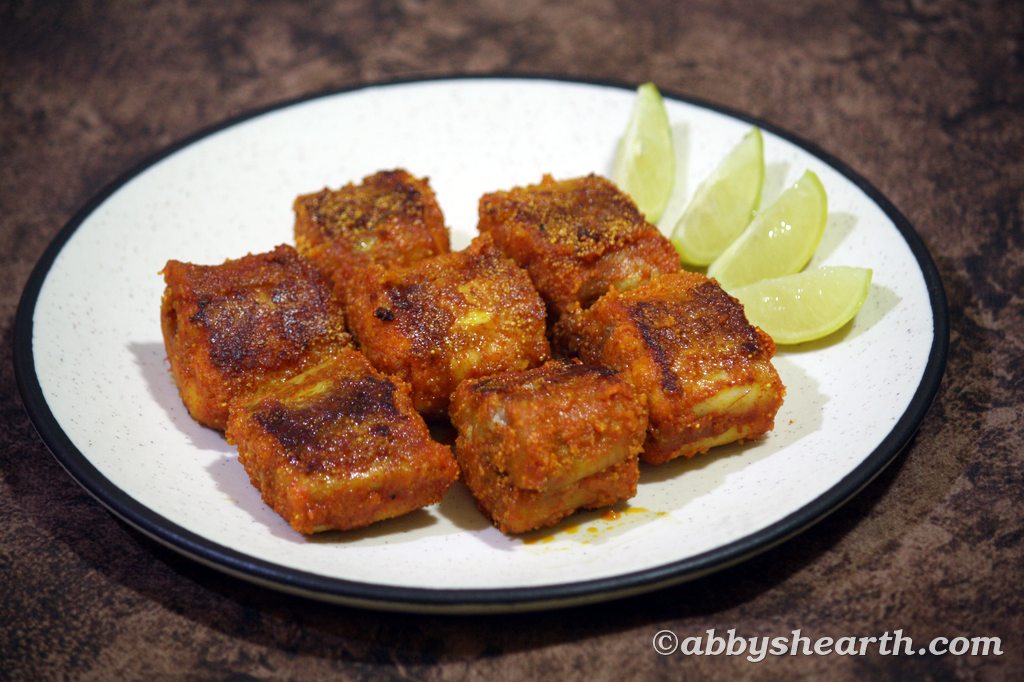 Crispy fried shark fish cubes with lime wedges on a beige plate.