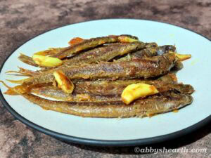 Crispy fried creek fish with garlic slices on a white plate.