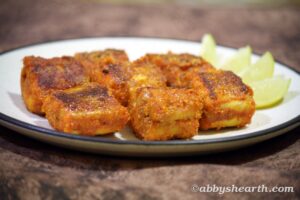 Crispy fried milk shark fish pieces served with lemon wedges on a white plate.