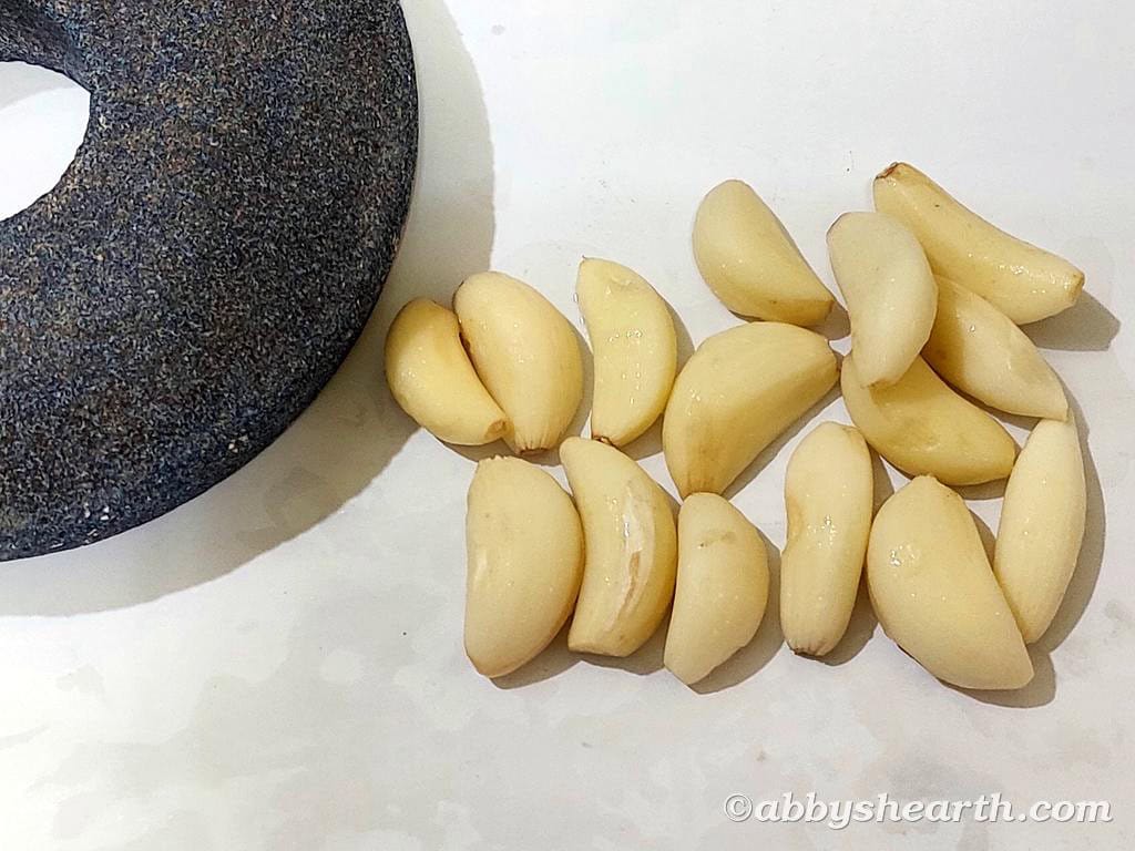 Fresh garlic cloves next to a stone grinder on a white surface.