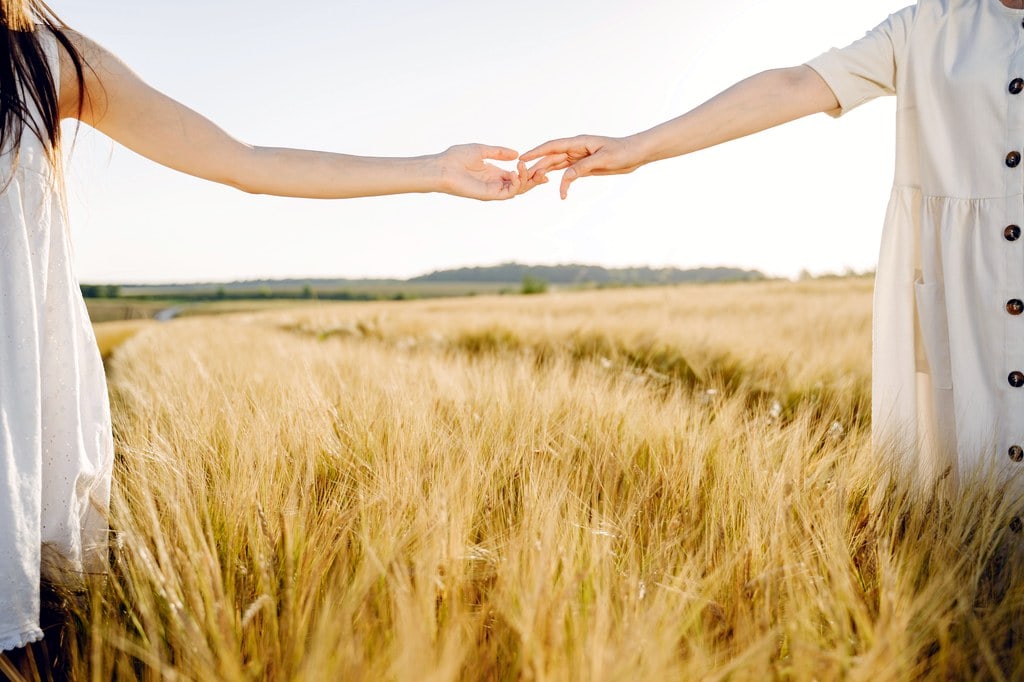 Two women with hands almost touching(letting go) in a field.