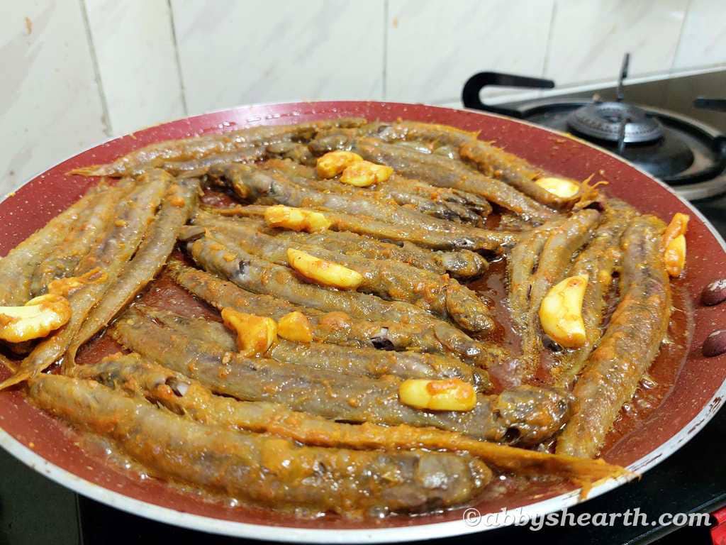 Crispy fried kalentas (fish) with garlic in a red skillet on stove.