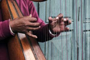 Worn hands playing a wooden harp.