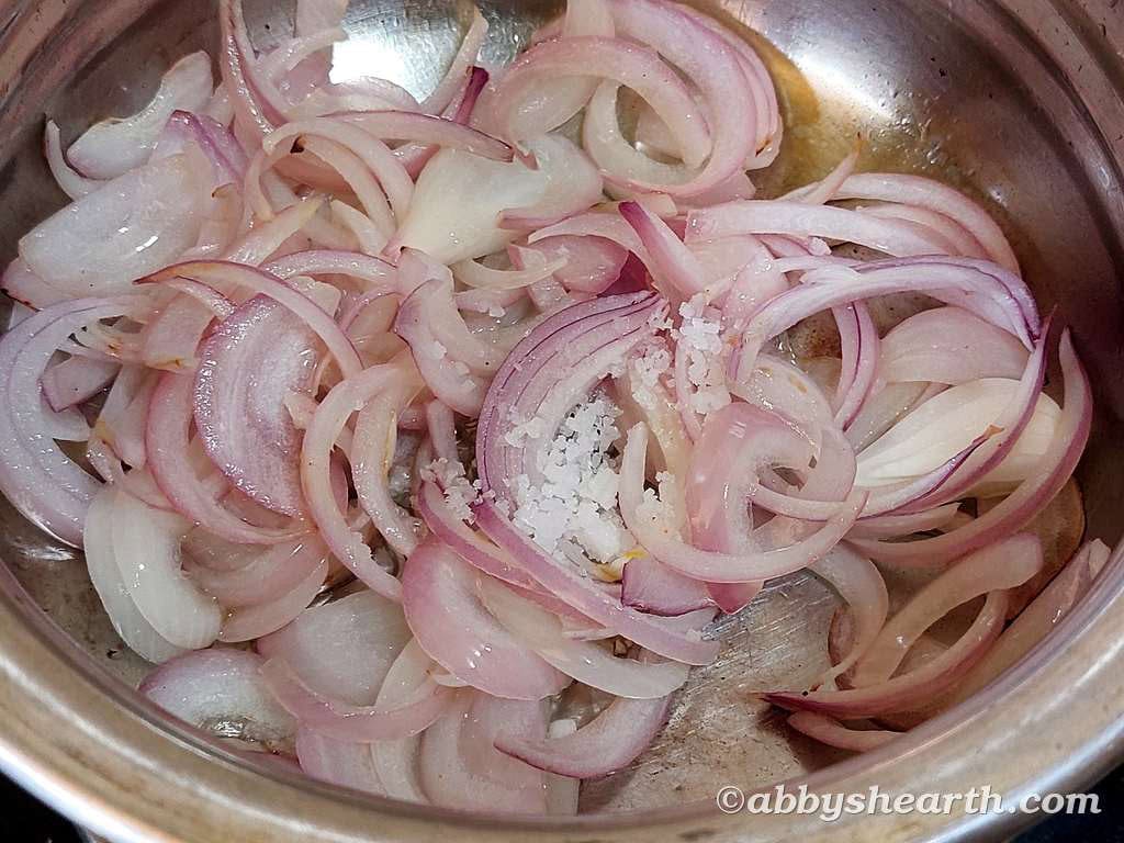 Sliced red onions cooking in a stainless steel pot for chicken liver stir fry.