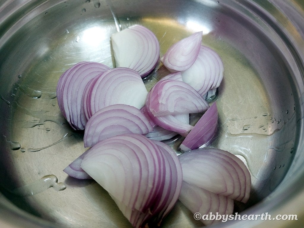Sliced red onions in a stainless steel bowl for cooking or recipe preparation.
