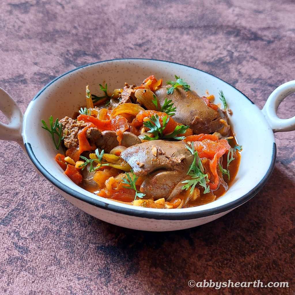 Chicken liver stir fry in a white bowl on a wooden surface.