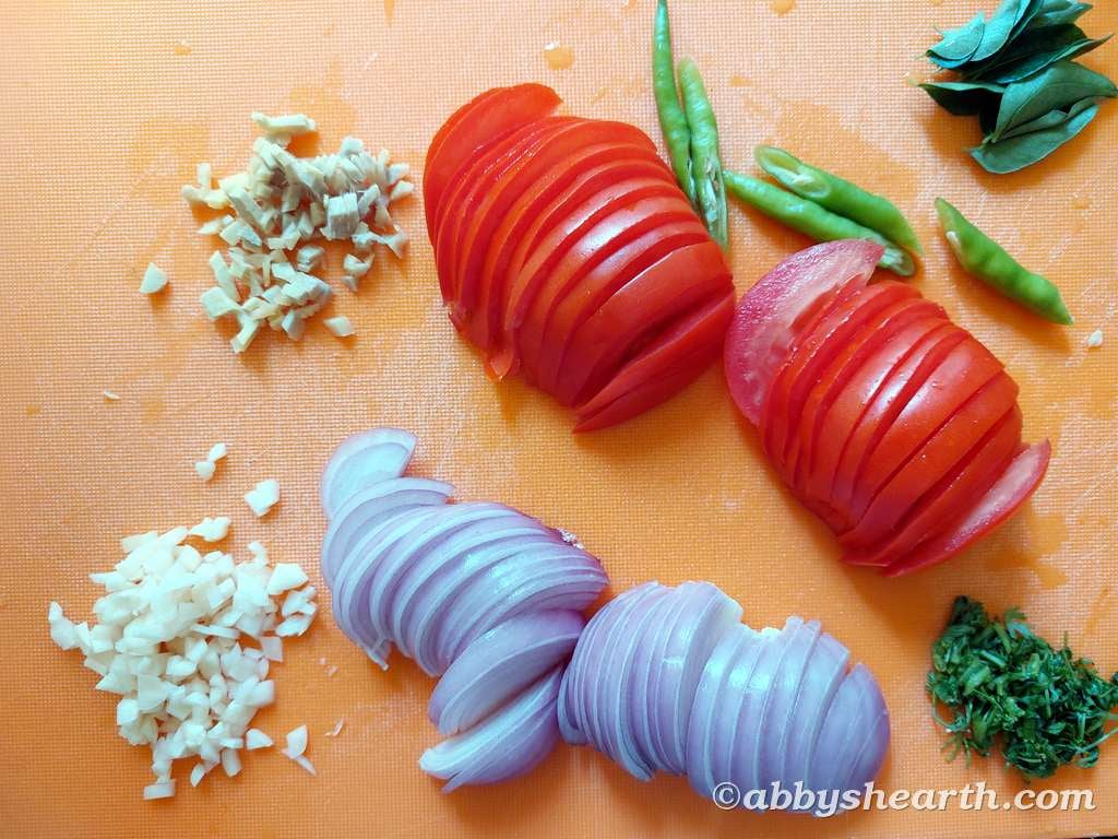 Sliced tomatoes, onions, garlic, and green chilies on a cutting board for cooking.