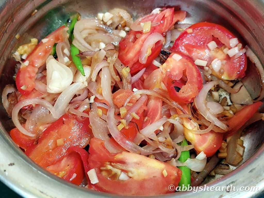 Onions, tomatoes and other ingredients cooking in a steel dish.