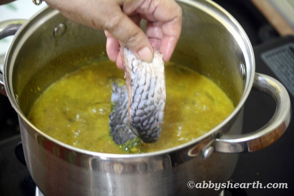 Mom starts adding illish fish pieces to the curry.
