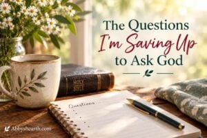 Notebook with questions, Bible, and pen on a wooden table with flowers in background.