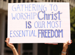 Hands holding poster with text "Gathering to worship Christ is our most essential freedom".