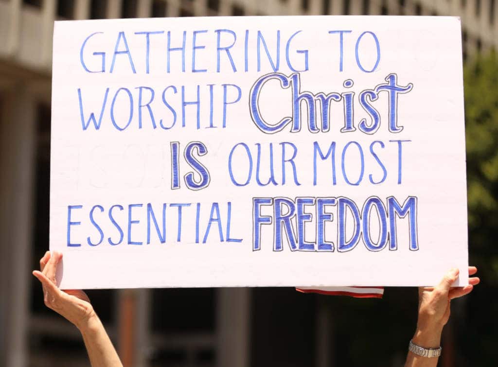 Hands holding poster with text "Gathering to worship Christ is our most essential freedom".