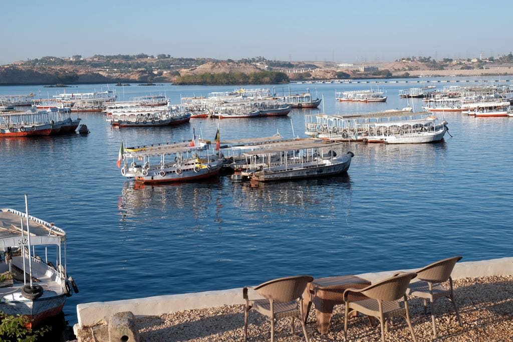 Boats docked at a harbor on the Nile River in Egypt with chairs on the shore.
