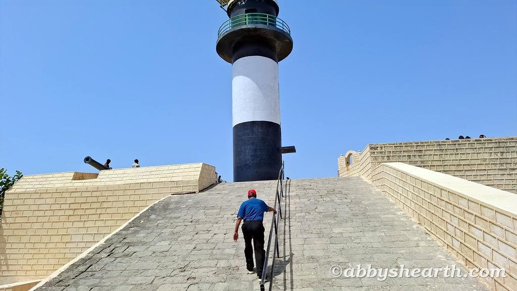 Climber ascending incline towards Diu Lighthouse on a sunny day.