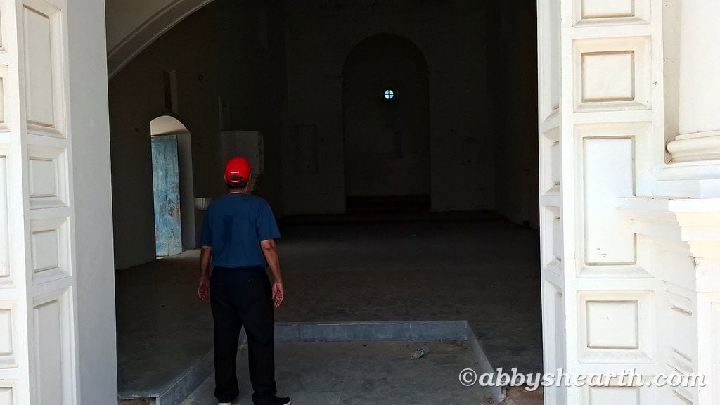 Old man in blue shirt and red cap exploring a historic church interior.