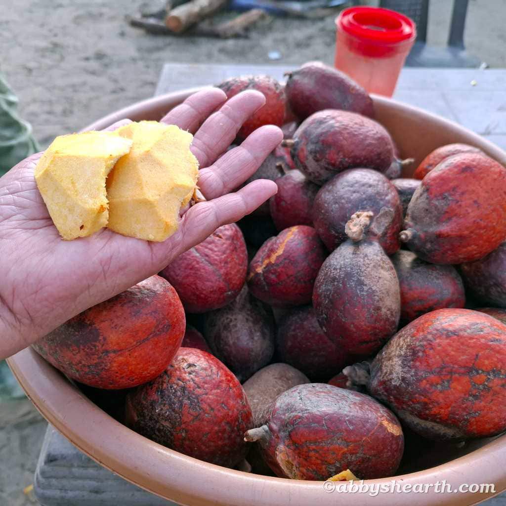 Hand holding a piece of hoka fruit over a basket of fresh hoka for sale.