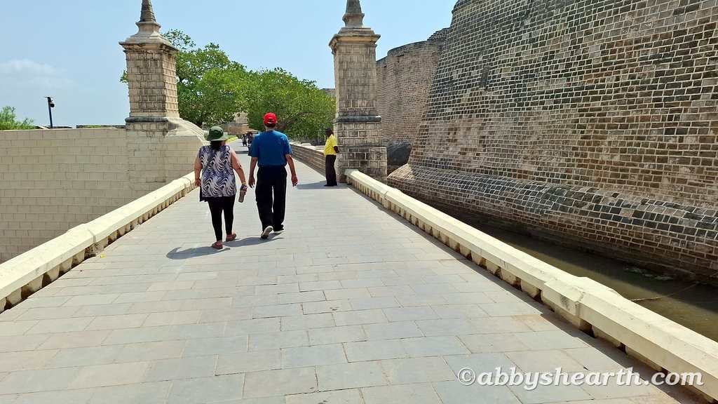 Tourists walking along the ancient fort wall in Diu with clear sky.