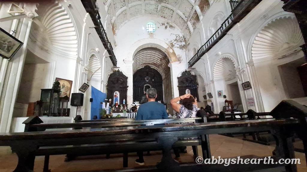 Visitors seated inside St. Paul's Church in Diu with high arched ceilings and religious artwork.