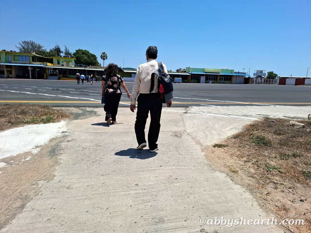 Parents walking on tarmac towards airport terminal in Diu, sunny day.