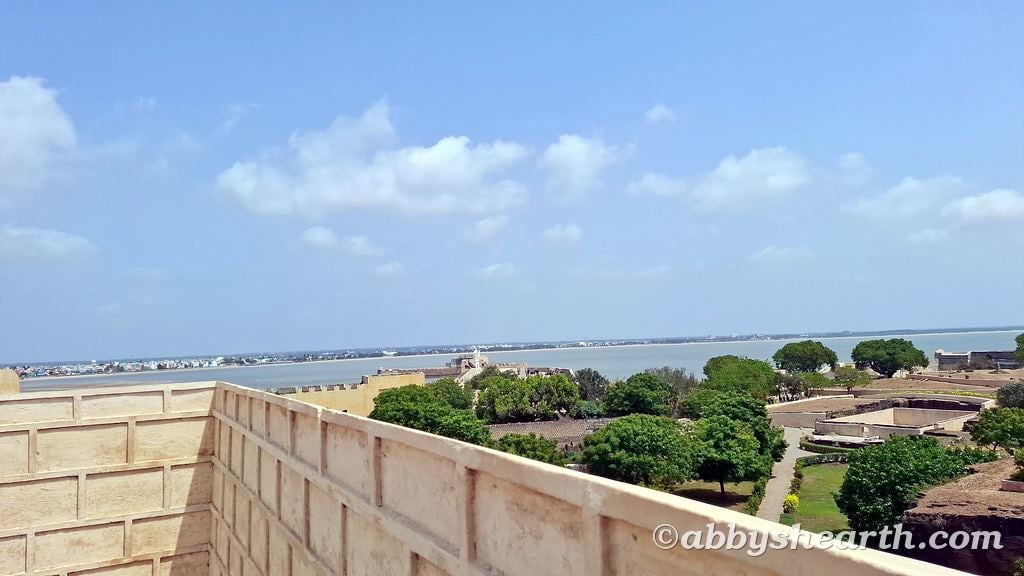 Scenic view of Diu coast with fort, trees, and blue sky.